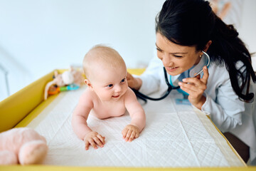 Happy pediatrician using stethoscope during baby's regular health checkup at doctor's office.