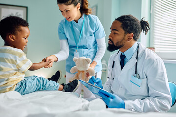 Small black kid shaking hands with nurse during medical checkup at doctor's office.