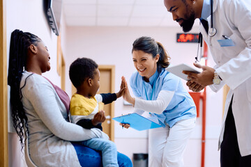 Happy nurse gives high-five to small black boy at medical clinic.