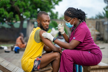 image of african guy receiving medical treatment from home- black nurse in facemask injecting a...
