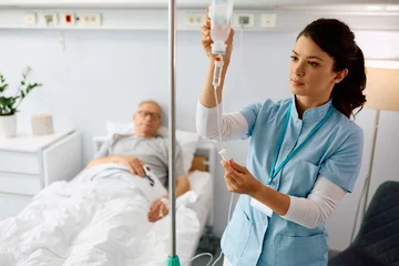 Fotobehang Nurse practitioner checking IV drip of senior patient at hospital ward. © Drazen