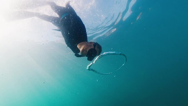 Free diver swims underwater in the murky sea and glides through the ring bubble. Freediver plays underwater with ring bubble