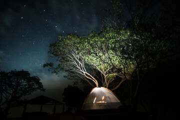 Man in a tent camping on Conchagua volcano under the stars in the night sky.