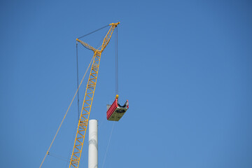 Crane lifting the nacelle to install it onto the tower of a wind turbine on a construction site, electricity, renewable energy and power concept, blue sky, copy space - obrazy, fototapety, plakaty