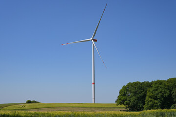 Tall wind turbine with a slender tower and three rotor blades standing on a field in a rural...