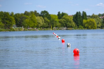 Floating balls in red and white mark the finish line on the lake during a rowing regatta, copy...