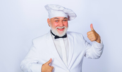 Smiling mature male chef showing thumbs up. Approve menu. Bearded cook in chef hat with perfect sign. Cooking concept. Professional chef, cook or baker in white uniform. Restaurant menu advertising.