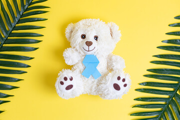 Teddy bear with blue ribbon and palm branches on yellow.