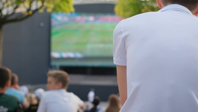 Little boy fan watching football match in fan zone, rear view