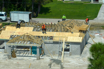 Aerial view of builders working on unfinished residential house with wooden roof frame structure...