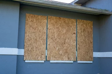  Boarded up windows with plywood storm shutters for hurricane protection of residential house. Protective measures before natural disaster in Florida © bilanol