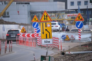 Roadworks warning traffic signs of construction work on city street and slowly moving cars