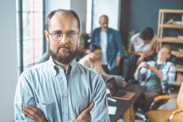 Team leader depicted through portrait of confident businessman, set against background of team working in office. Leader exemplifies qualities of leadership, professionalism, and business acumen. High