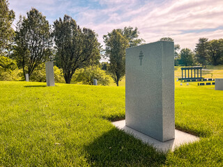 Focus on a single empty tombstone in a row of unmarked gravesites. The front of the stone is blank,...