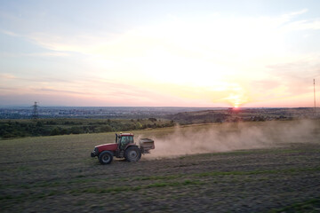 Tractor spraying fertilizers with insecticide herbicide chemicals on agricultural field at sunset