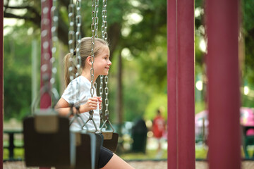 Young pretty smiling teenage girl playing alone on swings on summer playground