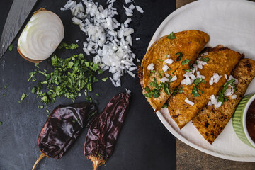 A plate of Mexican beef birria tacos of shredded beef, onions, guajillo peppers, cilantro, and broth with dipping sauce juices