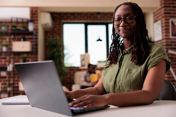 Company employee working remote typing casual smiling at camera while roommate enjoys free time at...