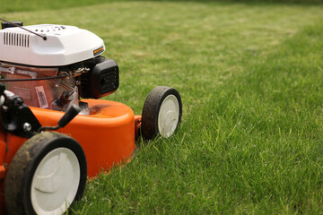 Gardening work tools. Close up details of orange electric lawn mower, wheels, motor on bright lush green grass. Rotary lawn mower machine cut lawn. Professional lawn care service. Place for text - obrazy, fototapety, plakaty
