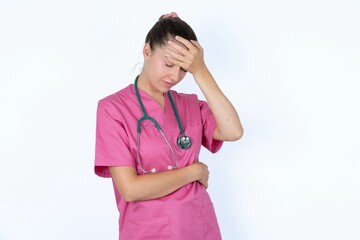 young caucasian doctor woman wearing pink uniform over white background making facepalm gesture...