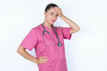 young caucasian doctor woman wearing pink uniform over white background touching forehead, hears something surprising, glad receive good news, feels relieved. Almost got in trouble.