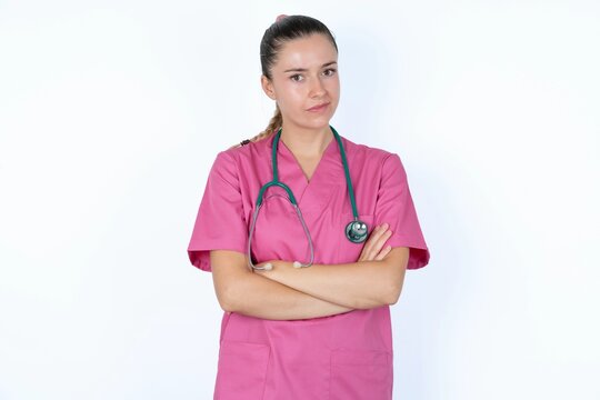 Picture of angry young caucasian doctor woman wearing pink uniform over white background crossing arms. Looking at camera with disappointed expression.