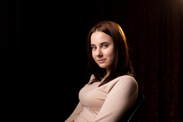 Fototapeta premium Portrait of a young woman on a dark background. The girl in the brown sweater. Friendly face looking at the camera.