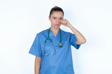 Disappointed dejected young caucasian doctor woman wearing medical uniform over white background wipes tears stands stressed with gloomy expression. Negative emotion