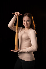 A young woman holds a bat in her hands and calmly looks into the camera. Black background....