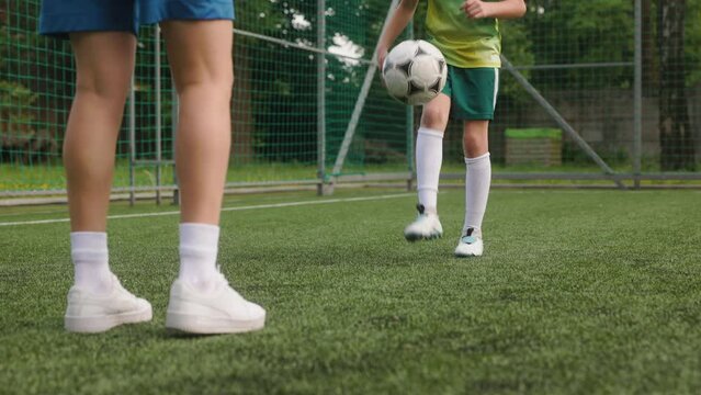 The female coach is training a young boy football player. The woman and the young footballer, dressed in football uniforms, are kicking up the ball to each other. close up of legs
