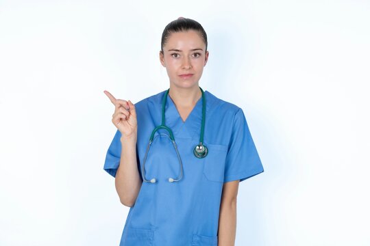 young caucasian doctor woman wearing medical uniform over white background points at copy space and advertises something, advices best price.