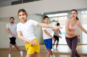 Portrait of cheerful teen girl practicing vigorous movements in dance class with brother and parents. Family active lifestyle concept
