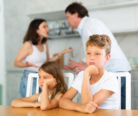 Family problem, conflict and people concept - sad children sitting at the table their parents quarreling at home