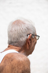 portrait of an elderly man in his eighties with his back half turned, smiling, wearing glasses and...