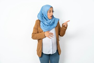 Stunned Young beautiful pregnant muslim woman wearing hijab over white background with greatly...