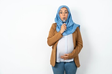 Photo of dreamy Young beautiful pregnant muslim woman wearing hijab over white background lick fork...