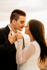 Pareja recien casada tocando la punta de la nariz felices con la luz de la puesta de sol, con anillo de matrimonio en la mano de ella