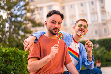 Fototapeta premium Smiling wedding couple eating a lollipop in the park on sunset in the city. Diversity and lgbt lifestyle concept