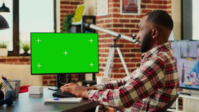 Focused freelancer cross checking information, transcribing data from chroma key mock up computer green screen to notebook. Concentrating teleworker remotely working in welcoming stylish apartment