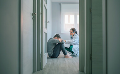 Female doctor reassuring and helping with empathy to male patient sitting on the room floor of a mental health center