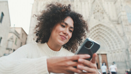 Close up, young woman scrolls on a cell phone. Happy girl uses mobile phone on old city background