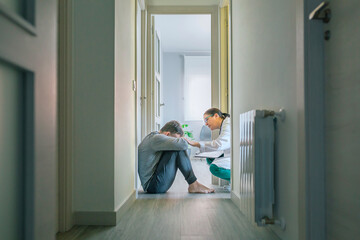 Female doctor reassuring and helping with empathy to male patient sitting on the room floor of hallway - obrazy, fototapety, plakaty