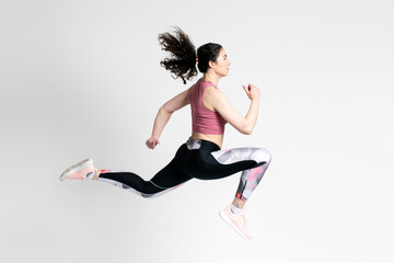 Female jogger in in pink top and shorts, running fast and jumping high up