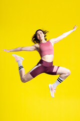 Fototapeta na wymiar Vertical studio portrait of a successful sportswoman jumping high up, looking at camera