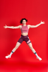 Young sportswoman looking at camera, performing stretching exercises and jumping high