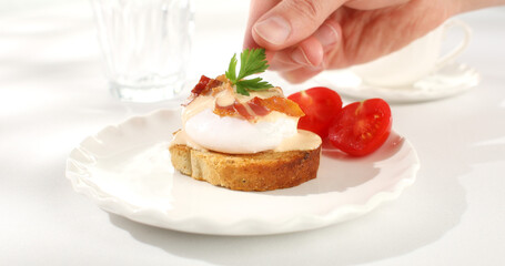 man decorates with greenery toast with poached egg and bacon on a plate. serving breakfast on a white background. sunny day. angle view. smooth zoom camera movement.