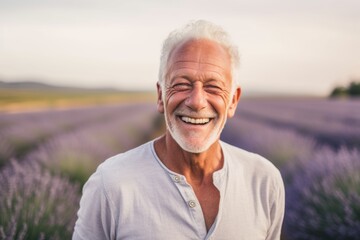 Fototapeta na wymiar Portrait of happy senior man standing in lavender field and laughing