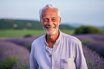 Fototapeta na wymiar Portrait of happy senior man standing in lavender field at sunset