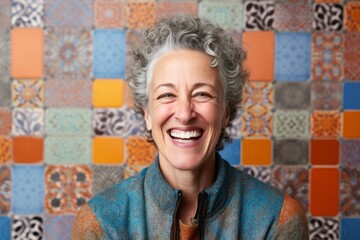 Obraz premium Portrait of a happy senior woman laughing against a colorful mosaic wall