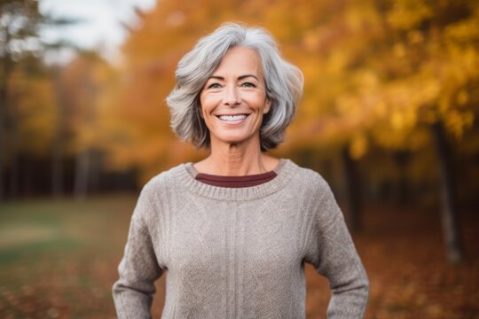 Portrait of smiling senior woman standing in autumn park and looking at camera